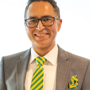 Head and shoulders photograph of a smiling man in a suit wearing glasses