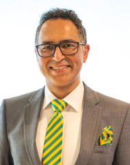 Head and shoulders photograph of a smiling man in a suit wearing glasses