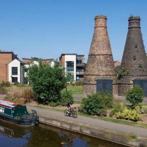Paul Barrett of Staffordshire University pictured cycling along Stoke-on-Trent's canal ways, flanked by pottery chimneys and a green barge.