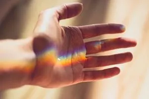 Open hand with a rainbow band of light across the palm and fingers.