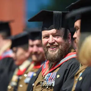 A smiling man in military uniform, wearing a graduation cap and gown