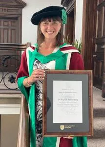 Dr Rachel Bolton-King holding her Outstanding Alumni Award certificate
