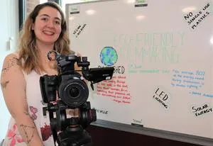 Film Production student Rebecca Head holding a camera in front of a whiteboard