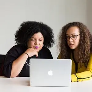 Two women sit at a laptop, with one pointing at the screen as they review results.