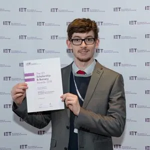 Young man in a suit holds an IET Engineering Horizons Bursary certificate.
