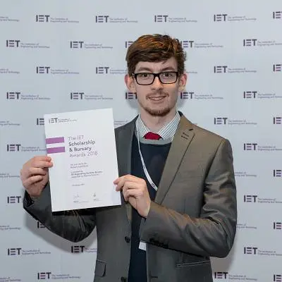 Young man in a suit holds an IET Engineering Horizons Bursary certificate.