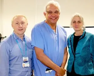 Three clinicians in blue and teal scrubs pose together in a hospital corridor.