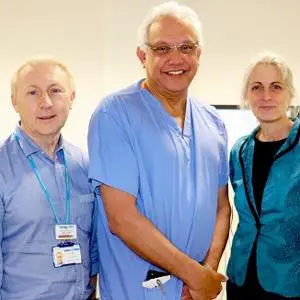Three clinicians in blue and teal scrubs pose together in a hospital corridor.