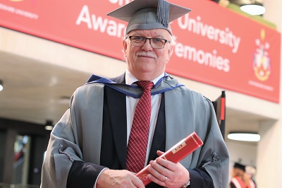 Ron Baldwin holding a scroll in his graduation robes
