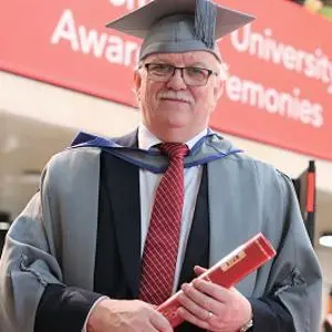 Ron Baldwin holding a scroll in his graduation robes