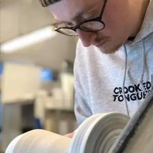 Student concentrates while shaping a ceramic vessel on a pottery wheel.