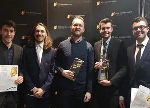 Five men pose at an awards backdrop holding trophies and certificates.