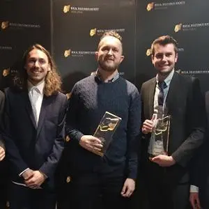 Five men pose at an awards backdrop holding trophies and certificates.