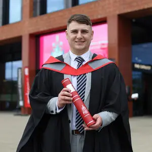 Ryan Zwetschnikow in his graduation robes holding a scroll