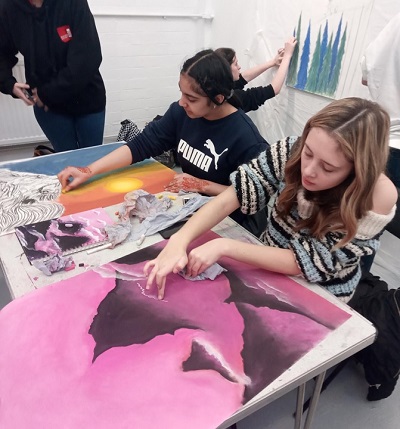 Students paint and assemble a large pink artwork at a shared studio table.