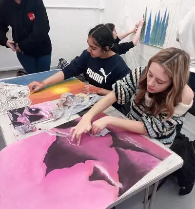 Students paint and assemble a large pink artwork at a shared studio table.