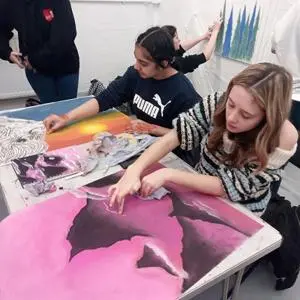 Students paint and assemble a large pink artwork at a shared studio table.