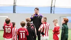 Football coach speaks to a group of children wearing red, white and green kits.