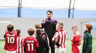 Football coach speaks to a group of children wearing red, white and green kits.