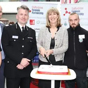 Six people, including police officers, pose behind an anniversary cake at a forensic partnership event.