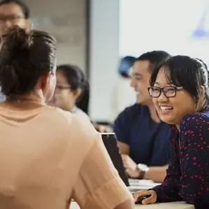 four people sitting and one standing in a classroom environment.