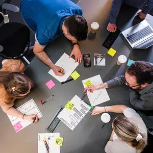 A bird's eye view of people working collaboratively at a table with laptops and sticky notes
