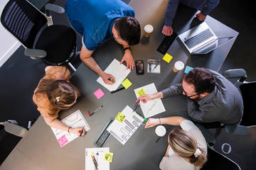 A bird's eye view of people working collaboratively at a table with laptops and sticky notes