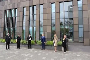 Six people stand spaced apart outside a modern brown-clad university building.