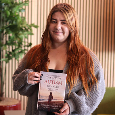 A women with long red hair smiling and holding a book