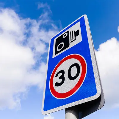 A blue road sign with a camera symbol and the number 30 in a red circle