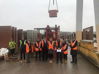 Construction team in orange high-visibility vests poses beneath a suspended precast panel.