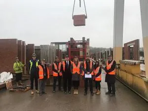 Construction team in orange high-visibility vests poses beneath a suspended precast panel.