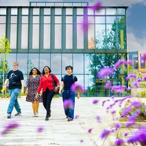 Four smiling students walking on front of a modern glass-fronted building.