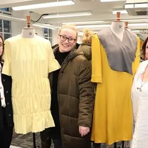 Three women stand beside mannequins dressed in cream and mustard sustainable garments.