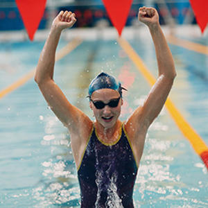 A young female swimmer in a pool with their arms raised in victory