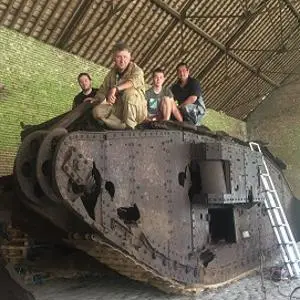 Four people sit and stand on a historic tank displayed inside a brick barn.