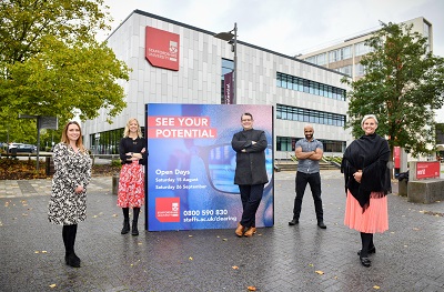 Four staff members stand outside a campus building beside a 'See Your Potential' sign.