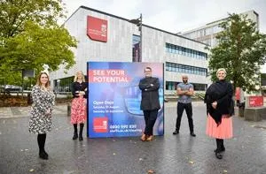 Four staff members stand outside a campus building beside a 'See Your Potential' sign.