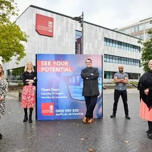 Four staff members stand outside a campus building beside a 'See Your Potential' sign.