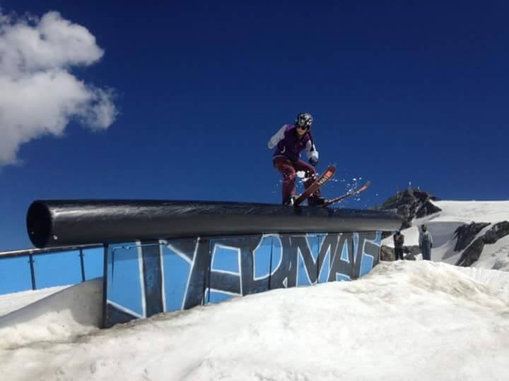 Freestyle skier slides along a black rail on a snowy slope beneath a deep blue sky.