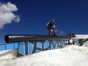 Freestyle skier slides along a black rail on a snowy slope beneath a deep blue sky.