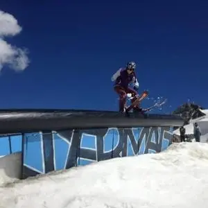 Freestyle skier slides along a black rail on a snowy slope beneath a deep blue sky.