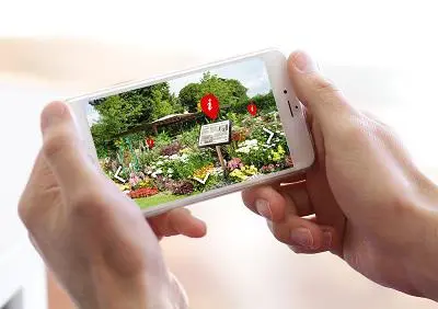 Hands hold a smartphone displaying an augmented-reality garden trail with red information markers.