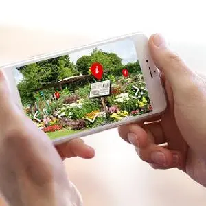 Hands hold a smartphone displaying an augmented-reality garden trail with red information markers.
