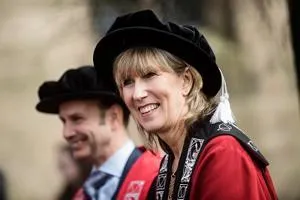 Smiling woman in red academic robes and a black velvet cap at a graduation ceremony.