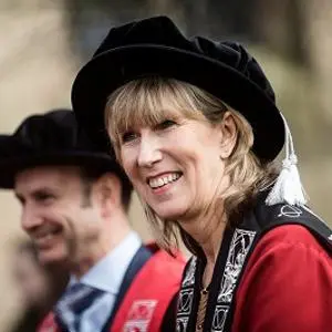 Smiling woman in red academic robes and a black velvet cap at a graduation ceremony.