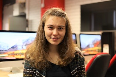 Young woman poses in a computer lab with multiple monitors behind her.