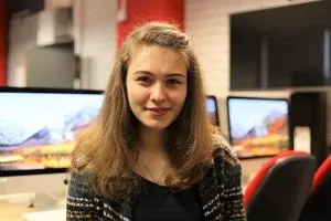Young woman poses in a computer lab with multiple monitors behind her.