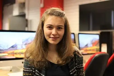 Young woman poses in a computer lab with multiple monitors behind her.