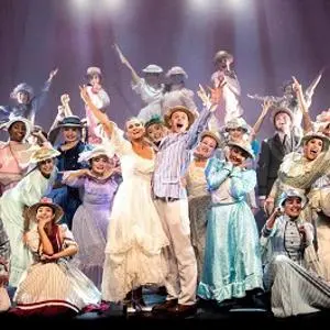 Large musical theatre cast in colourful costumes celebrates together on stage.